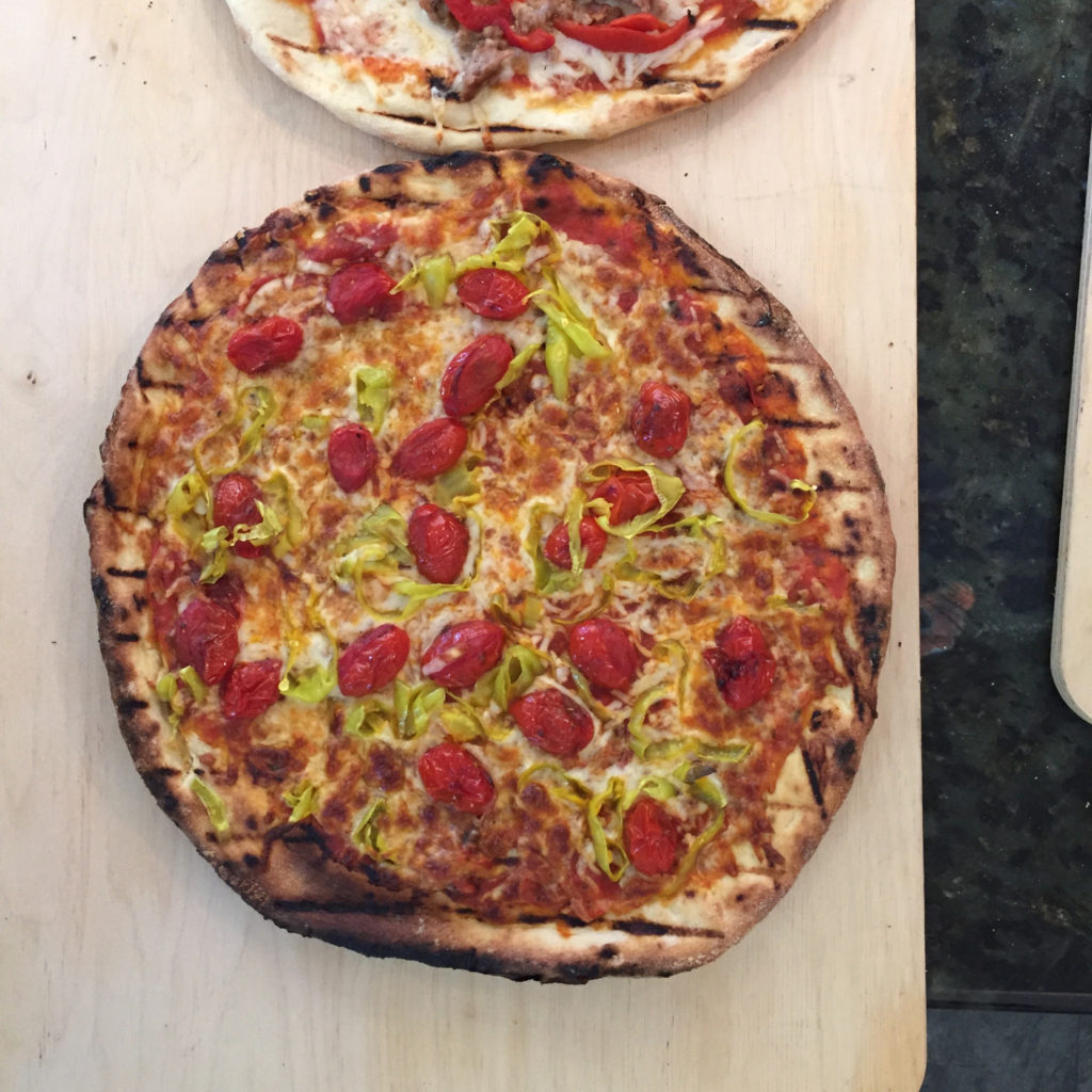 Grilled pizza topped with sliced cherry tomatoes, Sliced Golden Greek Peperoncini and Diced Sun-Ripened Dried Tomatoes. 